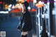 A woman in a black coat and hat standing on a city street.