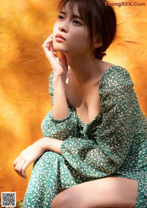 A woman in a green dress sitting on a stool.